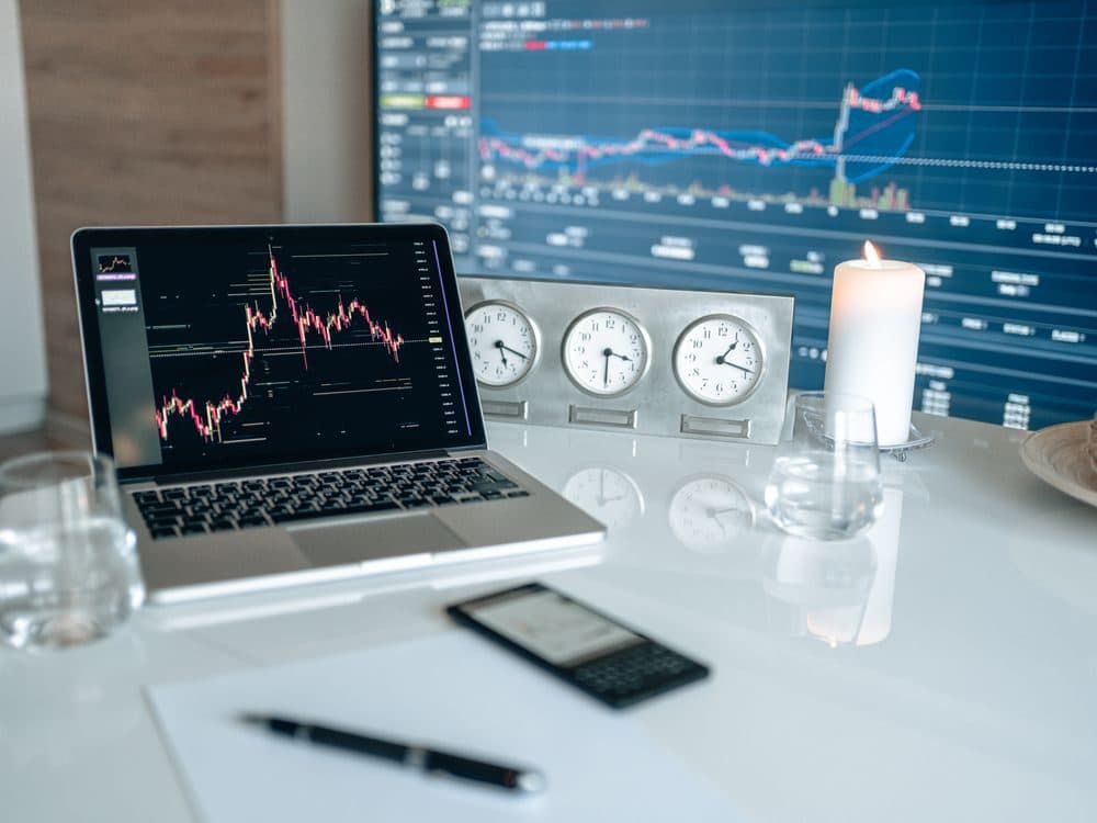 Live portfolio charts open on a laptop alongside world market clocks